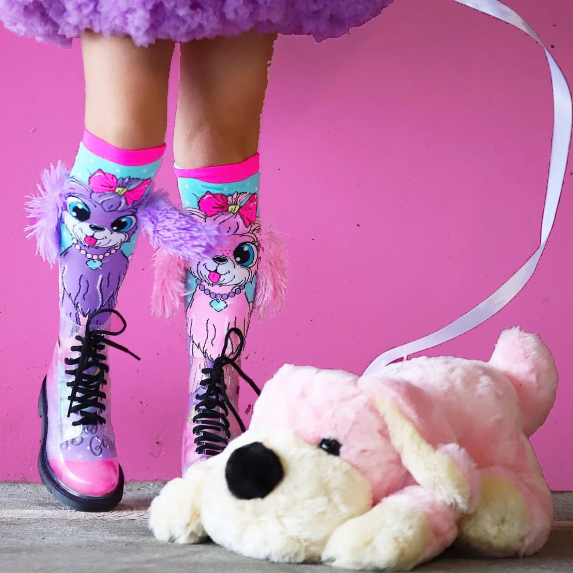 Mergaitė su MADMIA šuniukų kojinėmis ir rožiniu pūkiniu šuneliu ant pavadėlio