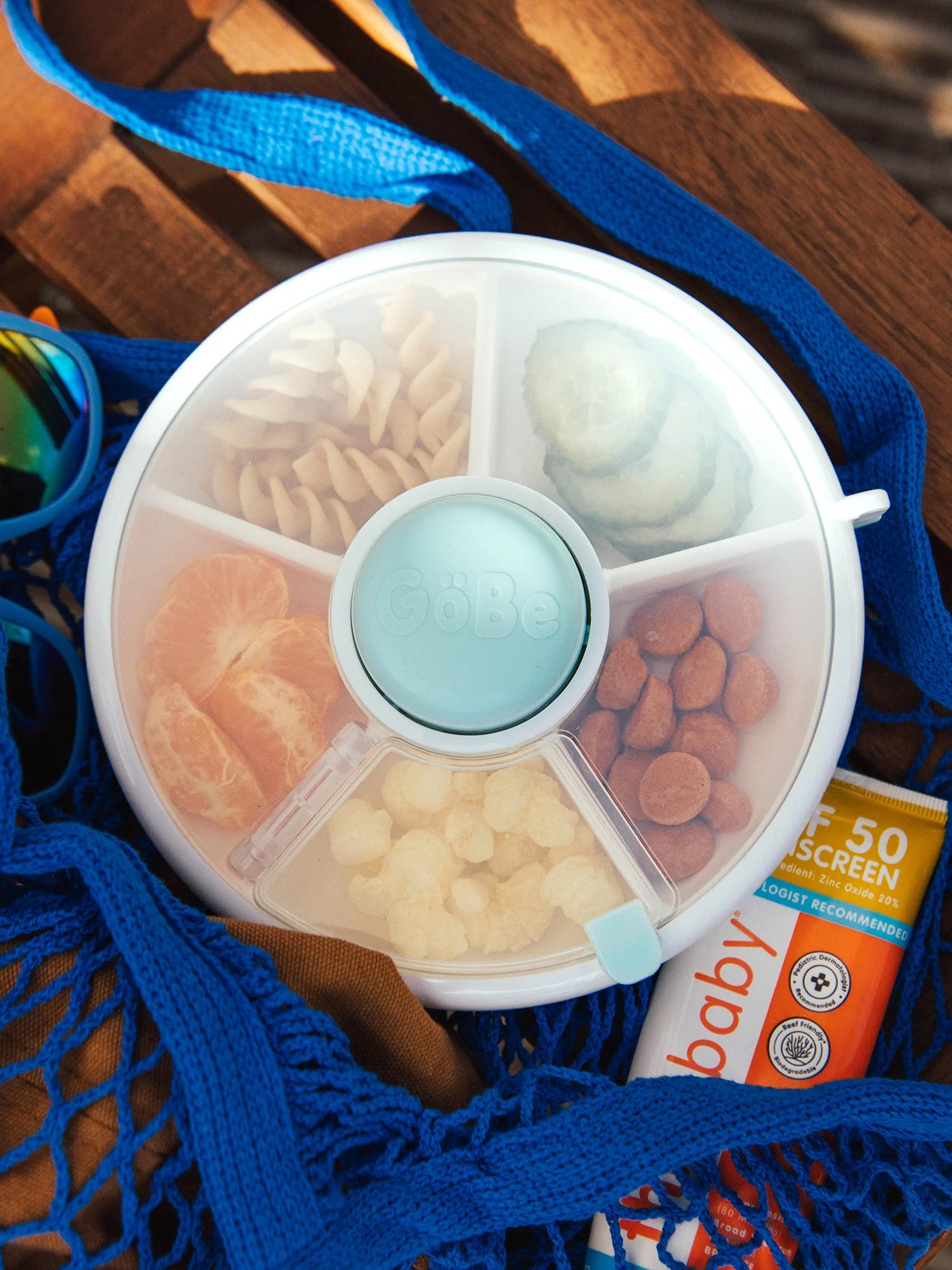GoBe Snack Spinner snack box in blue with compartments for fruits and snacks, resting on a wooden surface.