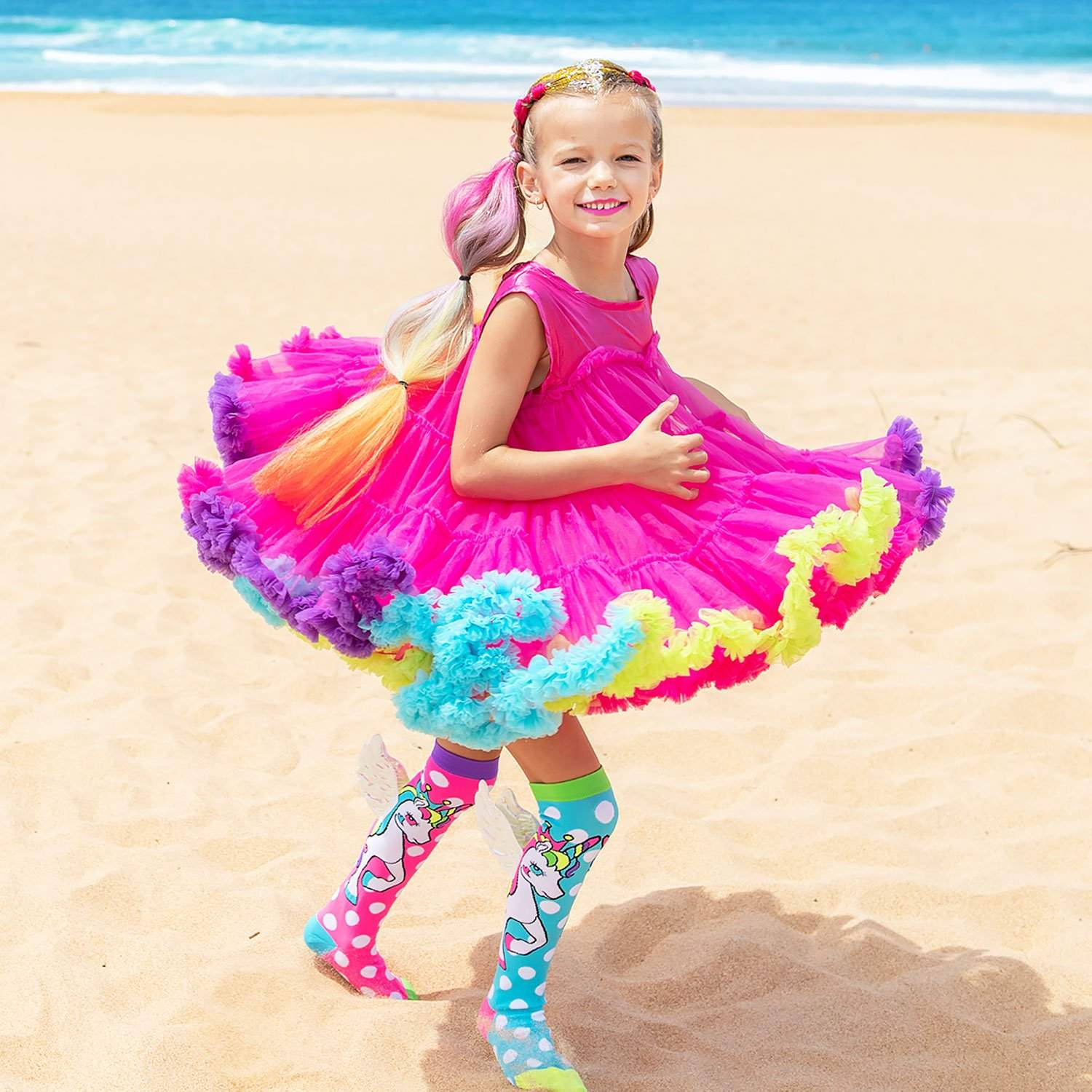 Girl in colorful pink dress twirling on the beach, wearing playful FLYING UNICORN socks.
